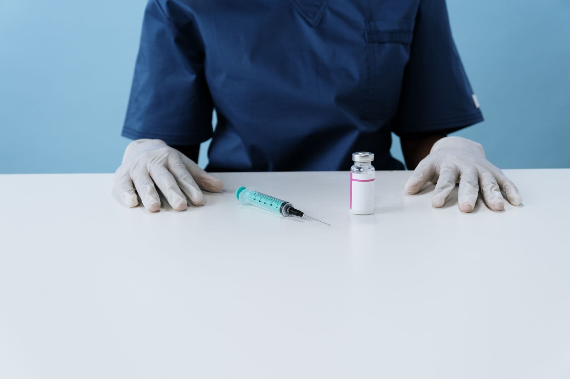 Medical professional wearing gloves with syringe and vial on a white surface.