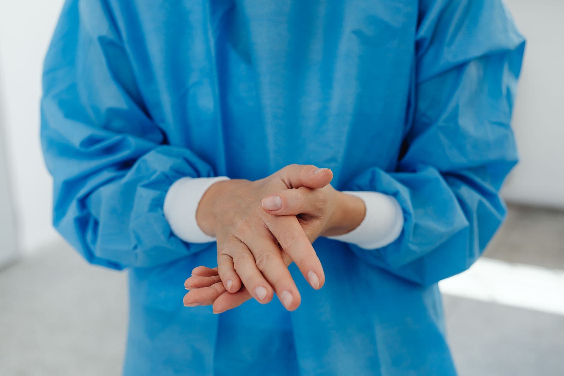Close-up of a healthcare professional wearing blue scrub suit with hands clasped.