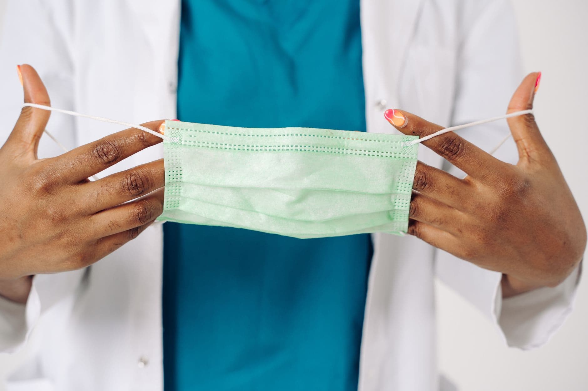 A healthcare worker demonstrates how to hold a surgical mask, emphasizing safety and hygiene.